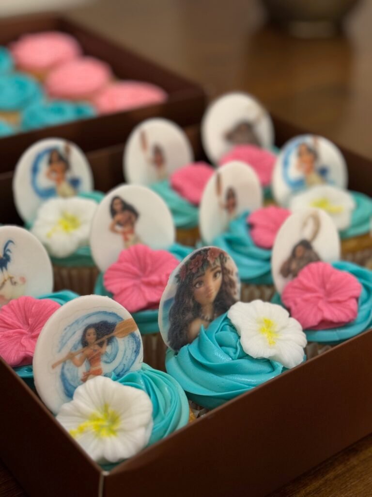 A box of custom Moana-themed cupcakes by Hala Cookies, featuring edible character prints and vibrant blue and pink frosting, perfect for kids' birthday parties in Doha.