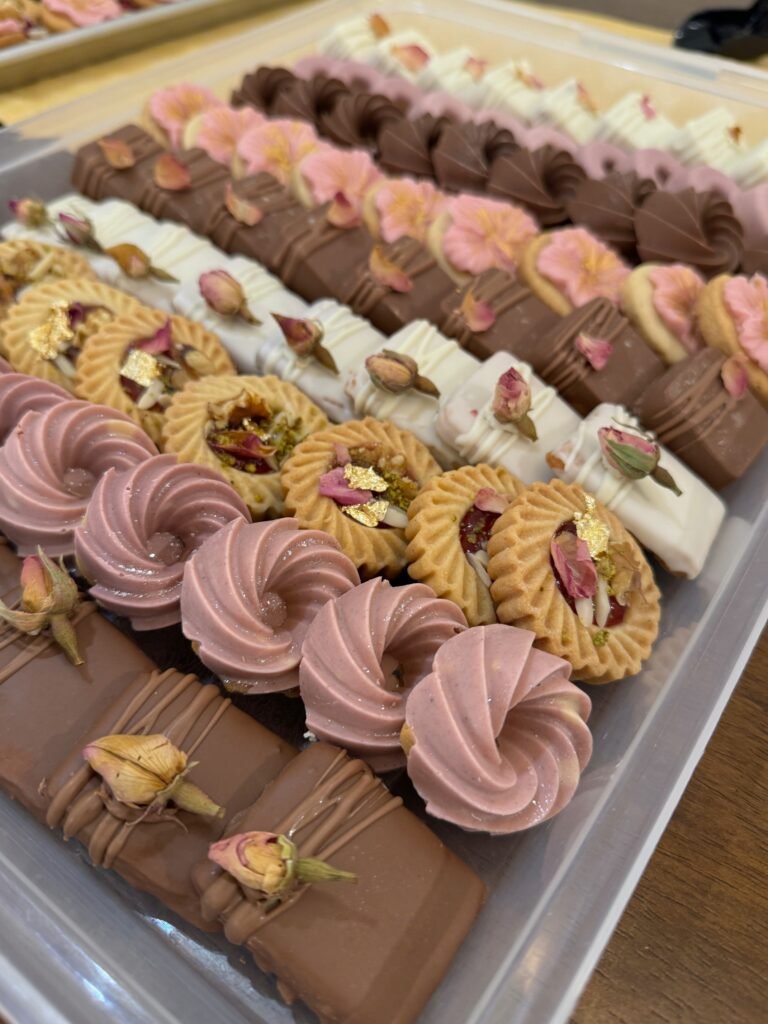 A large catering tray with an assortment of elegant petit fours by Hala Cookies, featuring chocolate, rose, and pistachio flavors, perfect for large events and weddings in Doha.