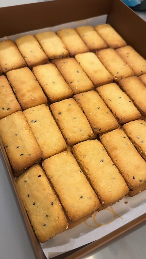 A box of freshly baked traditional biscuits by Hala Cookies, toasted sesame and aromatic black nigella seeds, a savory treat perfect for sharing with family and friends in Doha.